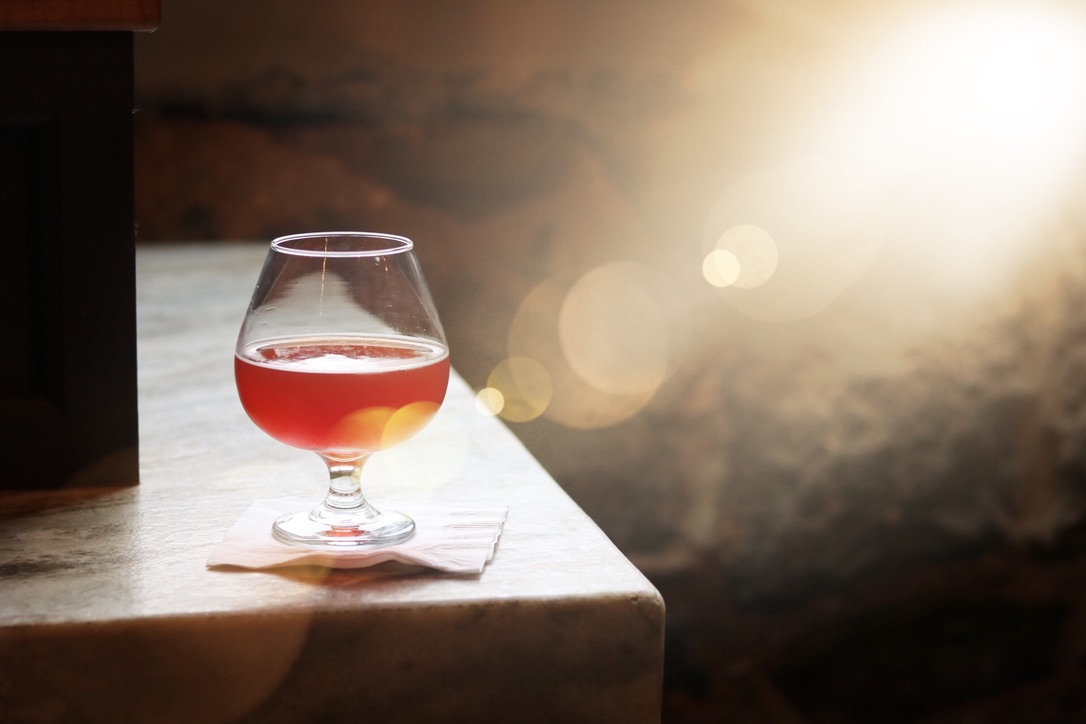 amber colored beer in snifter glass on bar's edge with beam of light and lens flare